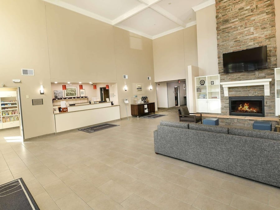A spacious lobby with a reception desk, a seating area with a grey sofa, a fireplace, and a kitchen area with a counter and shelves.