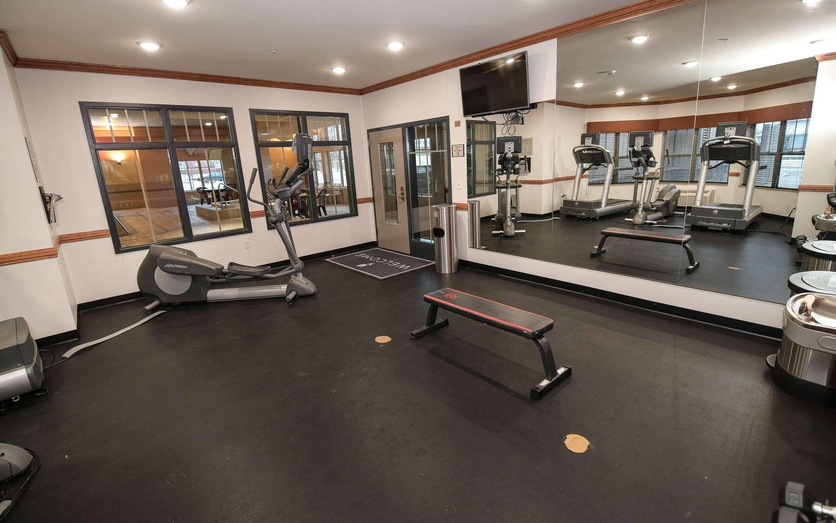 Une salle de sport équipée de matériel d’exercice, d’un banc et d’un grand miroir qui reflète l’espace.
