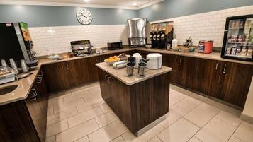 A modern kitchen with a central island, a coffee machine, and a refrigerator stocked with beverages.