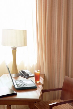 A wooden table with a laptop, a telephone, and a glass of iced tea. - Country Inn & Suites by Radisson, Grand Forks, ND (Grand Forks)