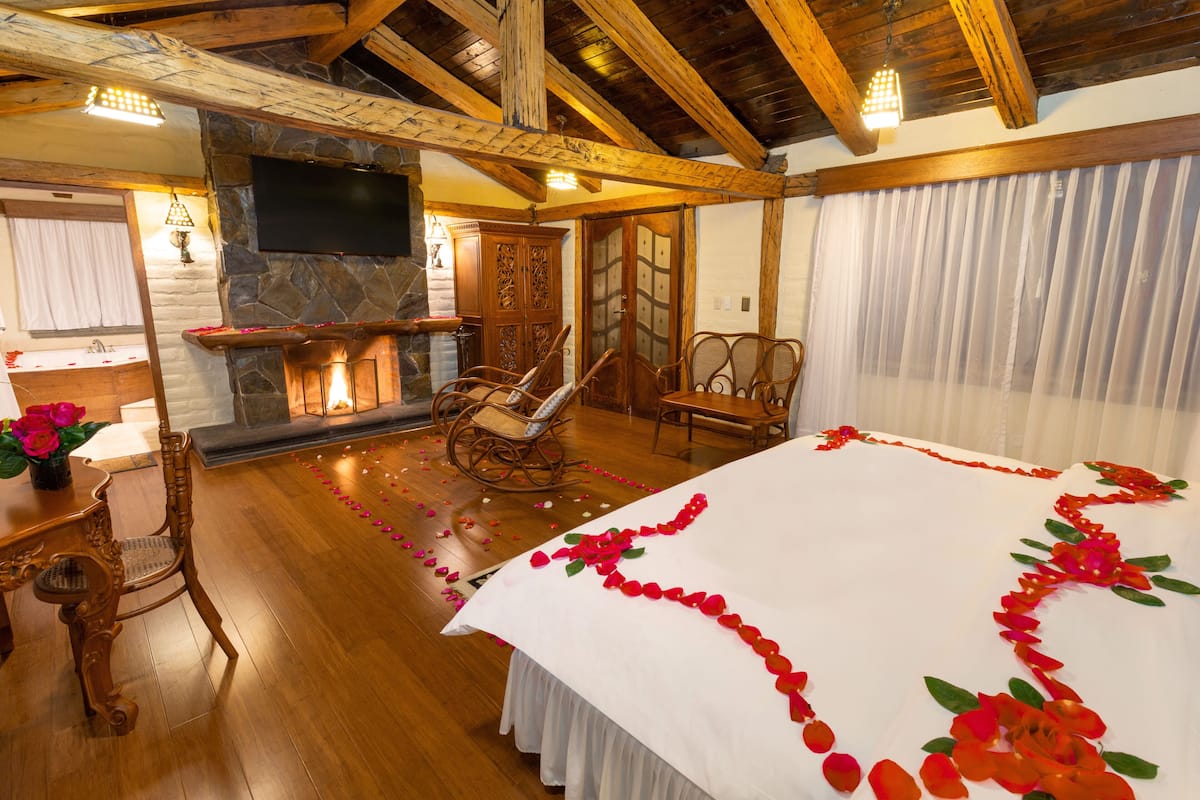 Ein Zimmer mit einem großen Bett, Holzboden, einem Kamin aus Stein, einem an der Wand befestigten Fernseher und einer Holzbalkendecke.