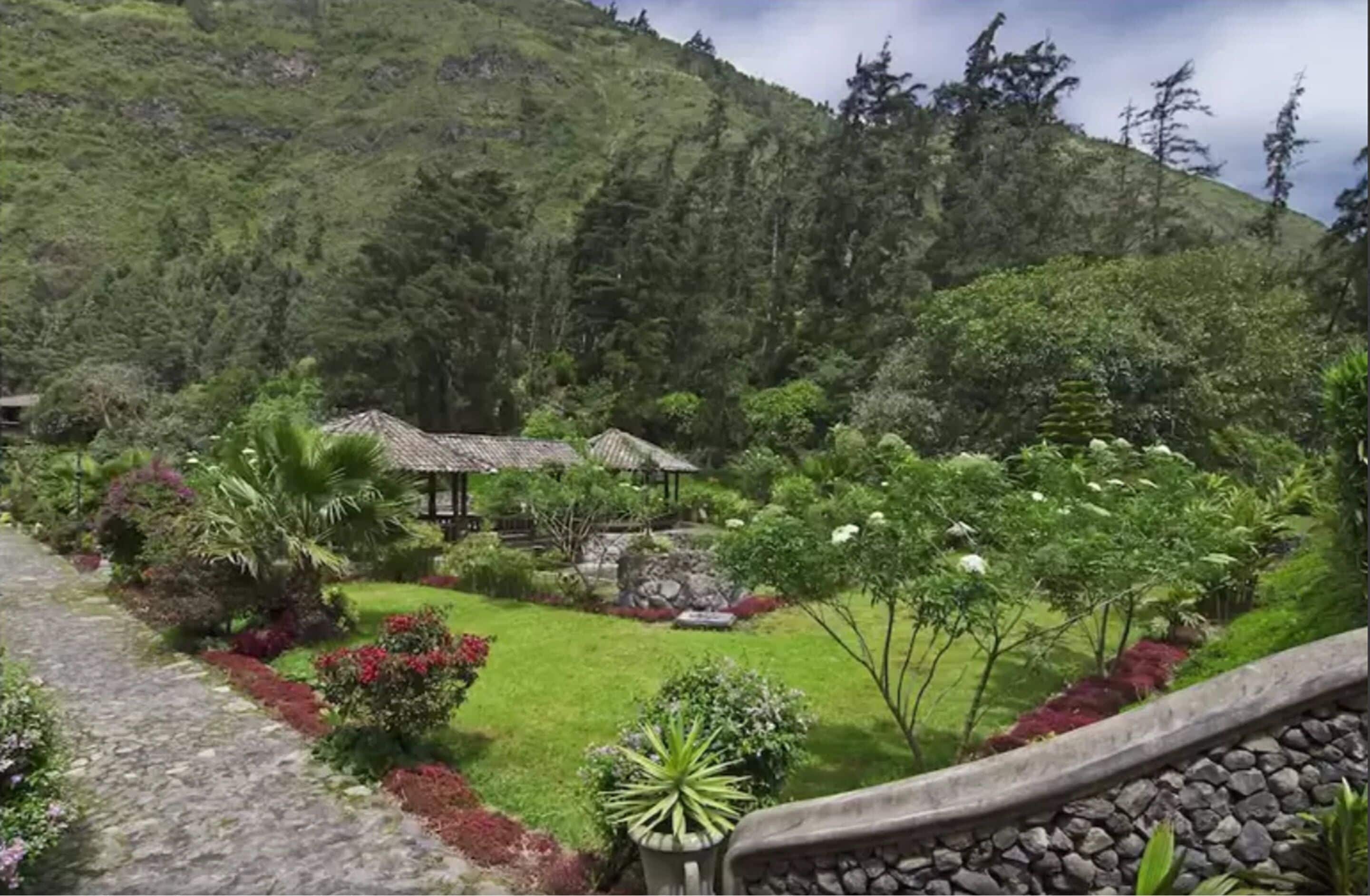 A lush garden with a gazebo, a stone pathway, and a mountainous backdrop.