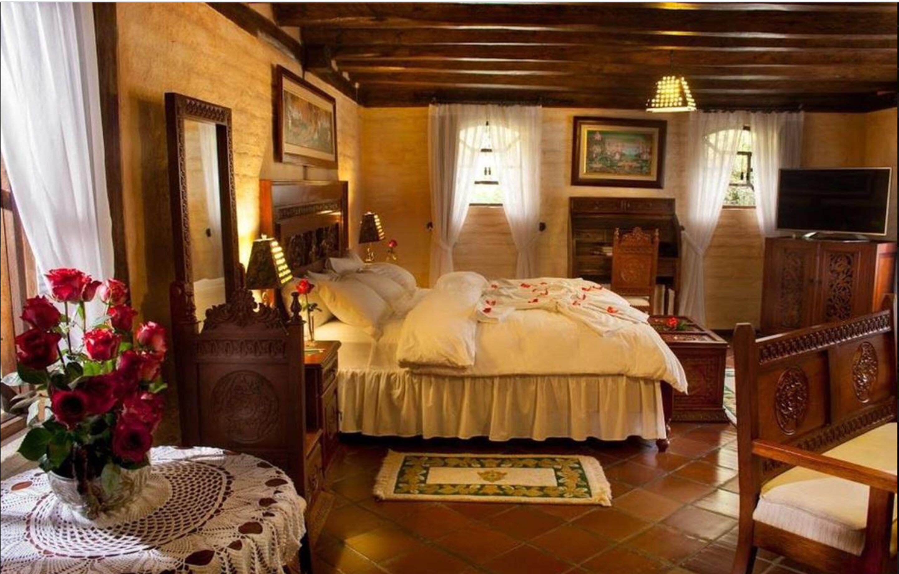 A traditional bedroom with a large bed, wooden headboard, a bedside table with a lamp, a mirror, and a television.