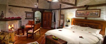 Una habitación tradicional con chimenea, una cama con ropa de cama blanca, muebles de madera y obras de arte en las paredes.