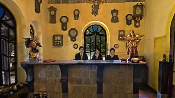 Un área de recepción con un mostrador de piedra, varios relojes y un amplio ventanal de arco.