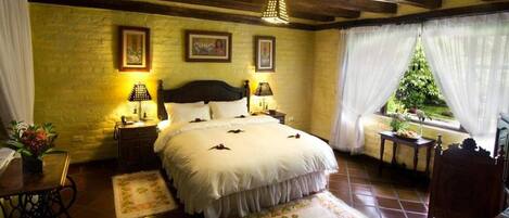 A bedroom with a large bed, two bedside tables with lamps, a window with curtains, and a plant on the windowsill.