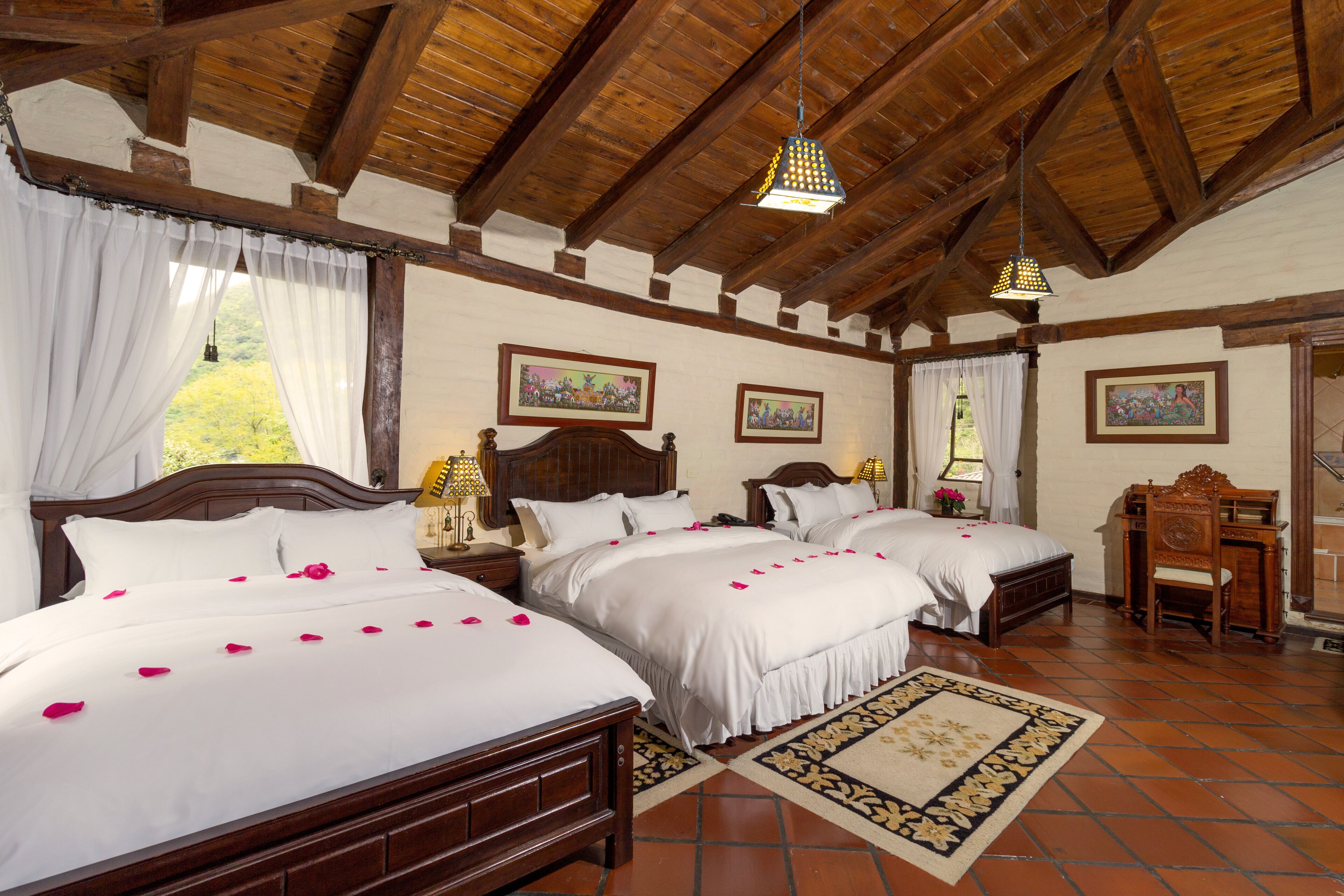 Habitación de hotel con dos camas grandes, cabeceros de madera, un escritorio de madera y un ventanal con cortinas.