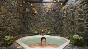 A stone-walled room with a bathtub, candles, and flowers.