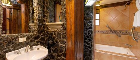 Un baño con pared de piedra, columna de madera, lavamanos y bañera con ducha.