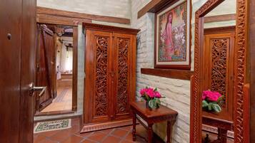 A room with a wooden wardrobe, a small table with a vase of flowers, and a framed picture on the wall.