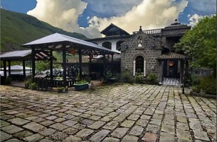 Un patio con pavimento de piedra, un pabellón y un pequeño edificio de piedra con un campanario.