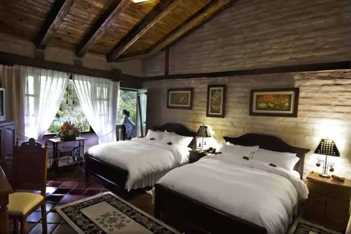 Ein Zimmer mit zwei Betten, Holzboden, Steinwand und einem Fenster mit Vorhängen.