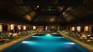 A large indoor swimming pool with lounge chairs and sunbeds around the perimeter.