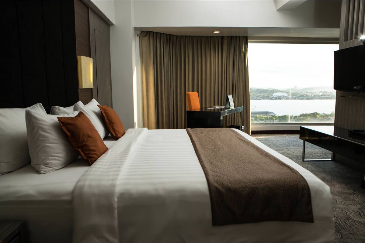 A hotel room with a large bed, a desk, a chair, a television, and a view of a body of water.