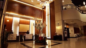 Een ruime lobby met een receptiebalie, een trap en een decoratieve plantenpresentatie.