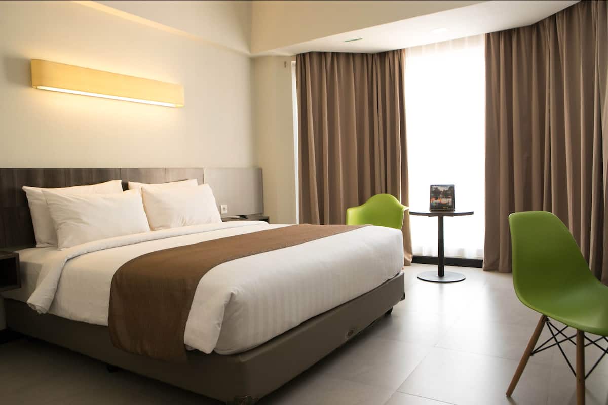 A hotel room with a bed, a nightstand, a table with a chair, and a window with curtains.