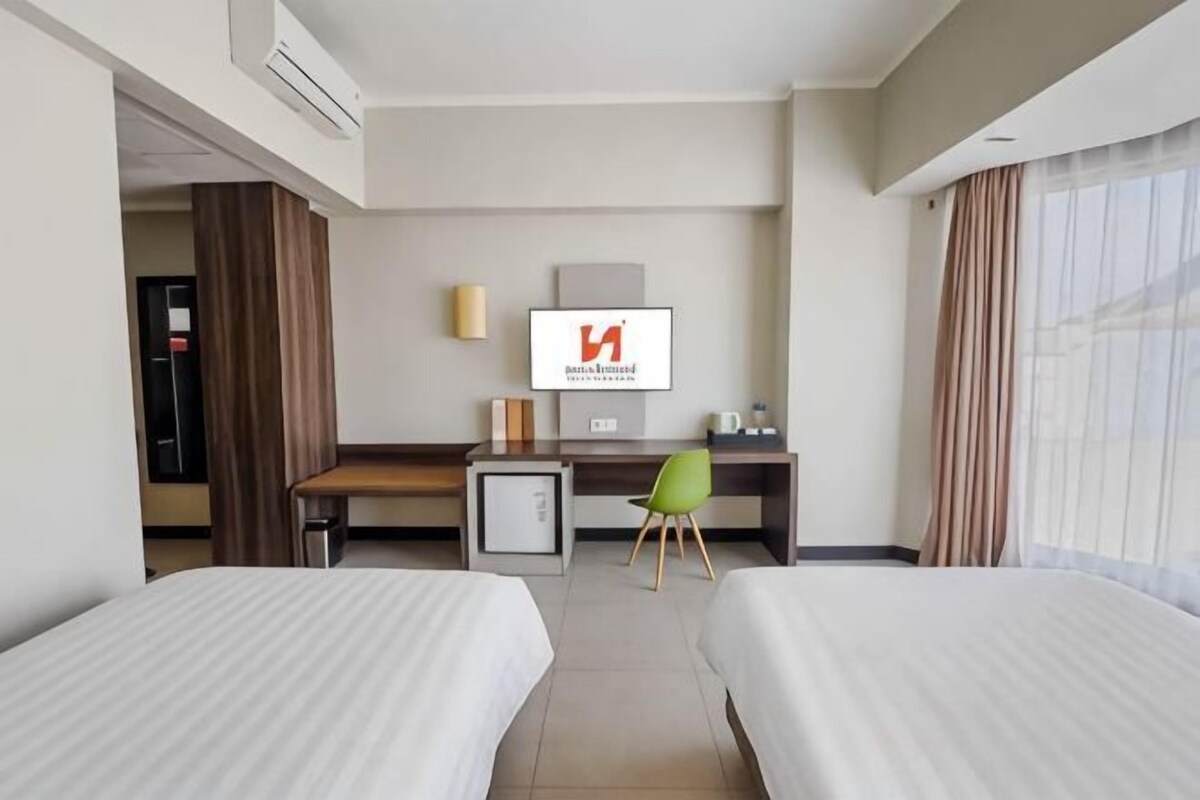 Une chambre d’hôtel avec deux lits, un bureau, une chaise, une télévision et une fenêtre avec des rideaux.