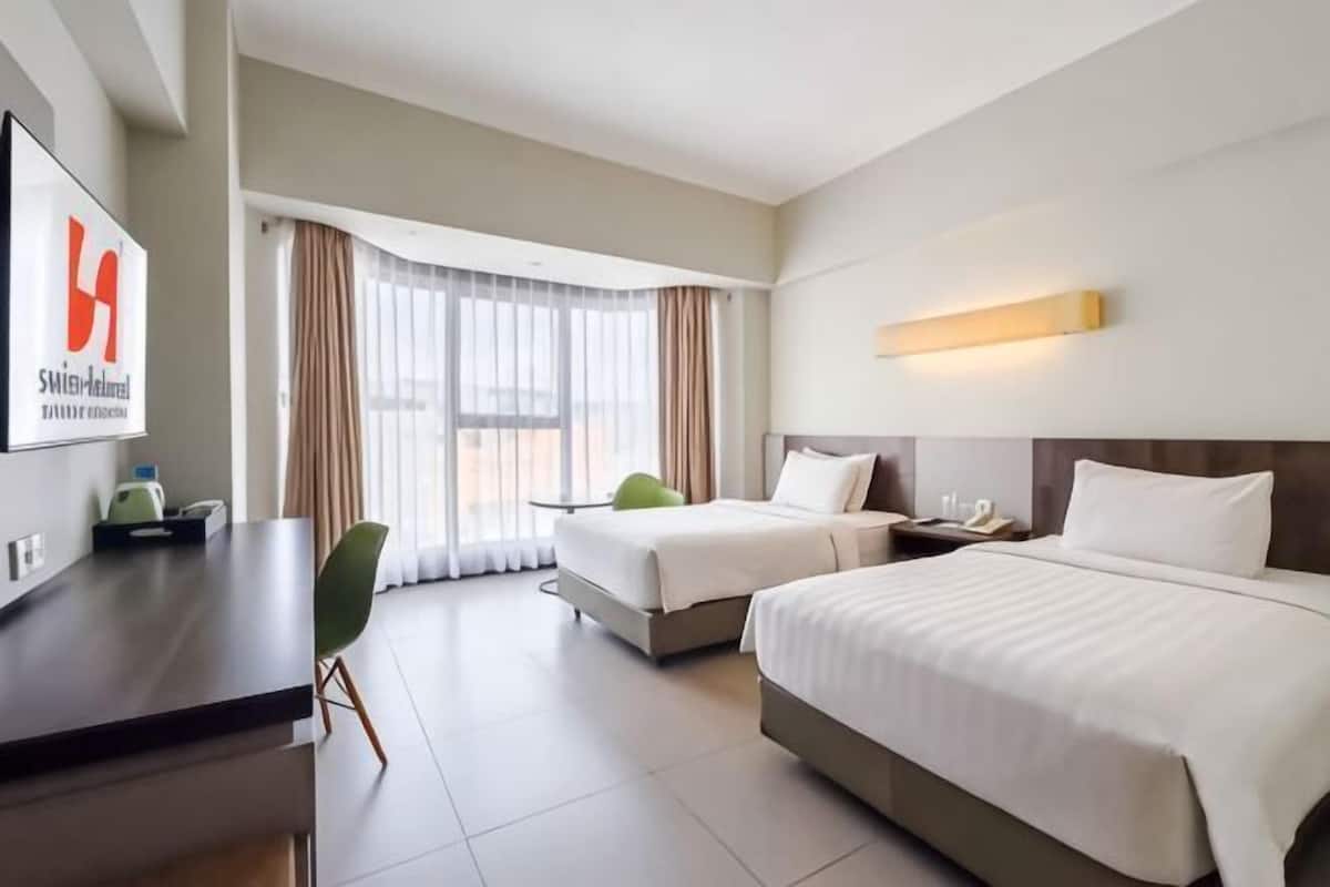 A hotel room with two beds, a desk, a chair, and a large window with curtains.