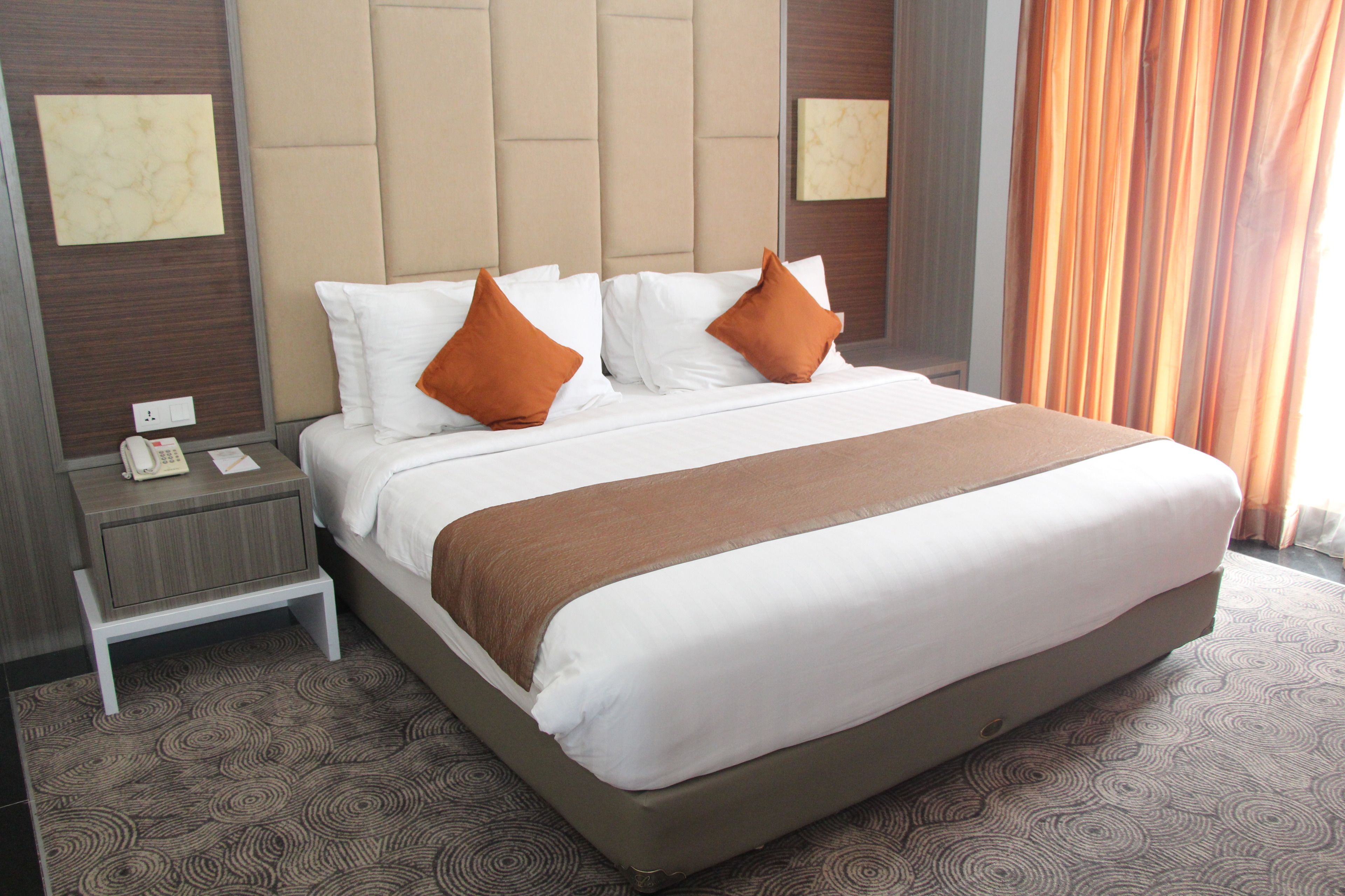 Habitación de hotel con una cama grande, dos almohadas, una mesita de noche, un teléfono y una obra de arte colgada en la pared.