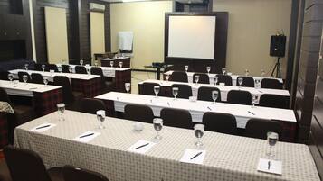 A conference room with multiple tables, each set with wine glasses and pens, and a large screen in the background.