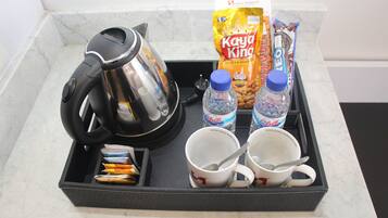 Un plateau contenant une cafetière, deux tasses, deux bouteilles d’eau, un sachet de cacahuètes grillées de la marque Kay King et des paquets de collations.
