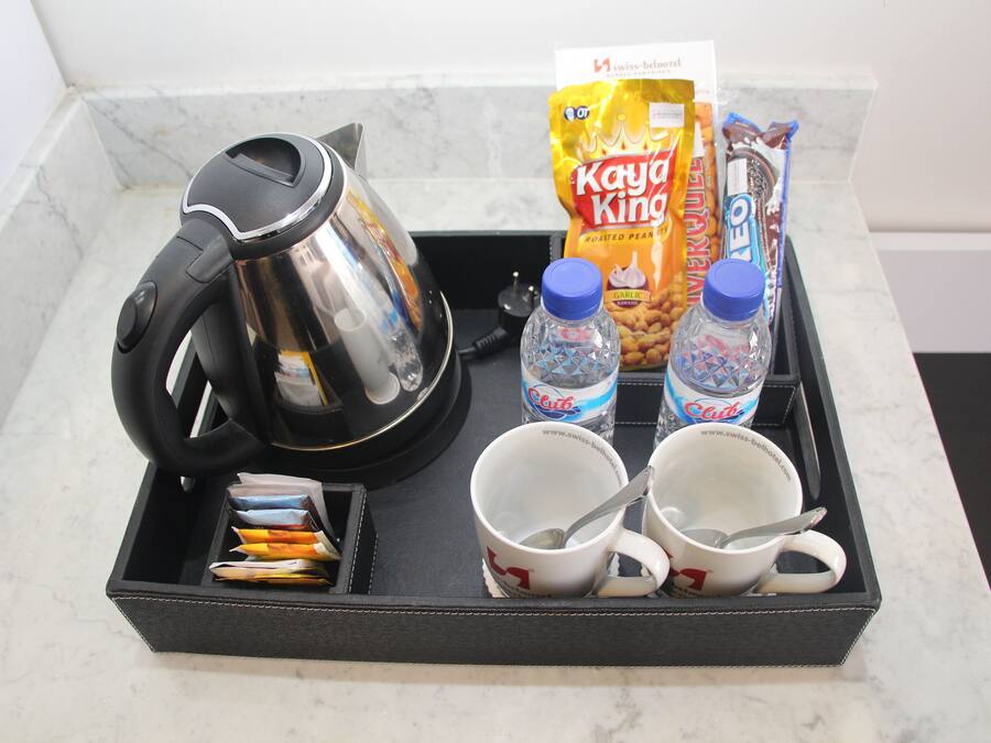 Un plateau contenant une cafetière, deux tasses, deux bouteilles d’eau, un sachet de cacahuètes grillées de la marque Kay King et des paquets de collations.