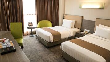 A hotel room with two beds, a desk, a chair, and a small table.