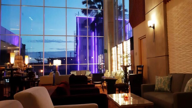 Een moderne hotellobby met een grote glazen wand, comfortabele zitplaatsen en uitzicht op een gebouw met paarse verlichting.
