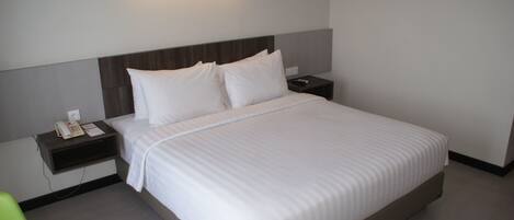 Una cama bien hecha con sábanas blancas, una mesita de noche con un teléfono y un bloc de notas, y una lámpara de pared sobre la cama.