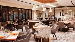 Een modern restaurant met meerdere eettafels, stoelen en hangende pendantlampen.