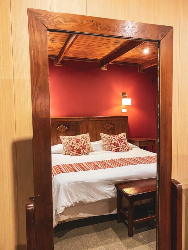 Une chambre à coucher avec une tête de lit en bois, un lit avec une literie blanche et des oreillers à motifs floraux, une table de chevet et une commode.