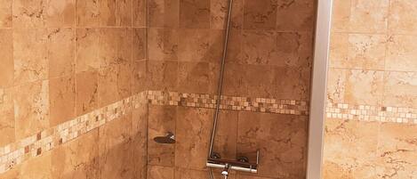 A corner shower with a handheld showerhead, a built-in seat, and a wall-mounted control panel.