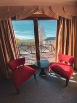 Una habitación con dos sillas rojas, una mesita y vistas al exterior a través de un ventanal.