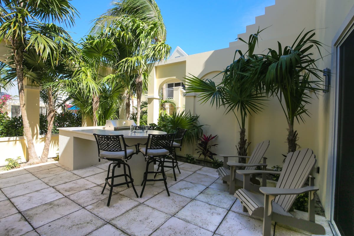 Une terrasse avec une table et des chaises, entourée de palmiers et de plantes en pot.