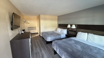 A hotel room with two beds, a desk, a mirror, and a wall-mounted TV.