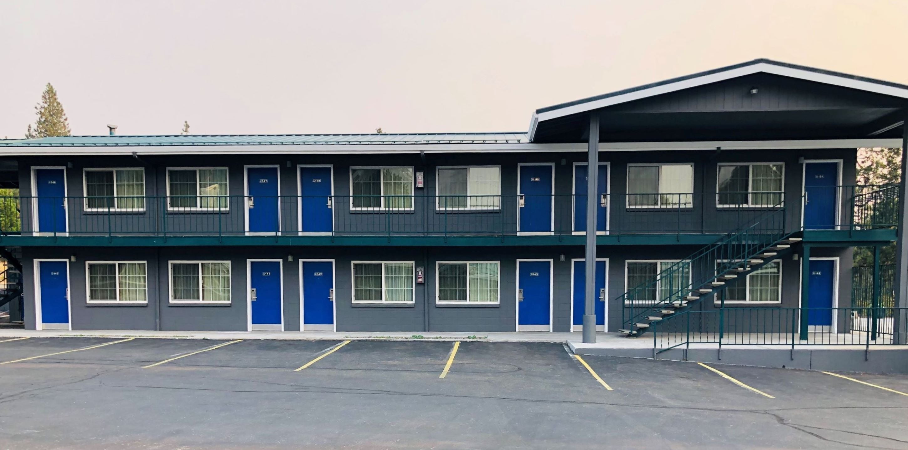 Um motel com vários quartos, área de estacionamento coberta e escada que leva a um andar superior.