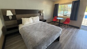 A hotel room with a large bed, two bedside lamps, a small table with two red chairs, and a window with curtains. - Pine Needles Inn (Mount Shasta)