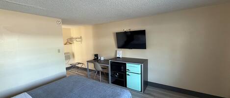 Een hotelkamer met een bed, een bureau, een stoel, een televisie en een kleine kitchenette.