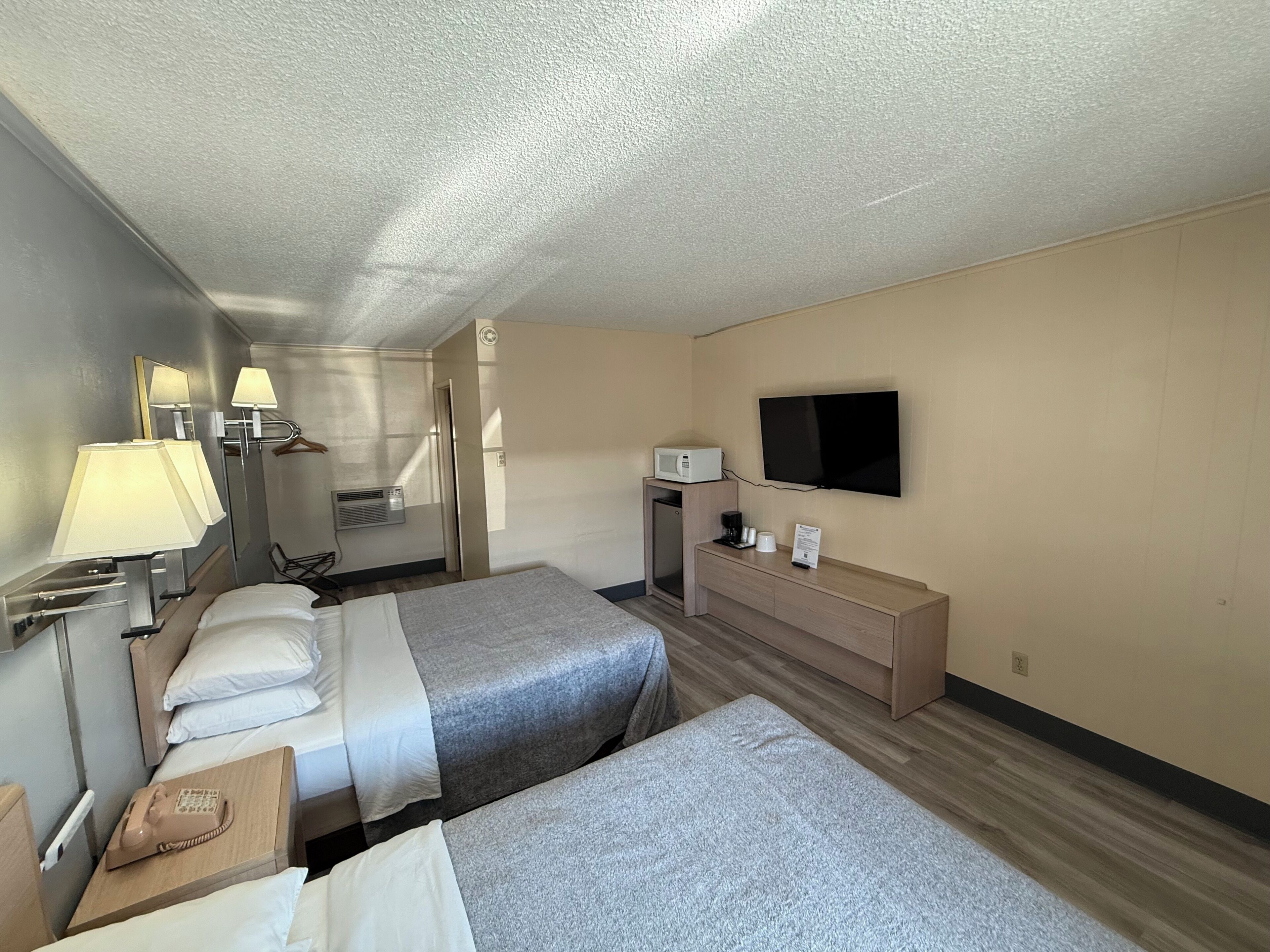 Et hotelværelse med to senge, et fladskærms-tv, minibar og et skrivebord med telefon.