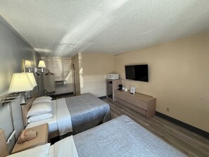A hotel room with two beds, a flat-screen TV, a minibar, and a desk with a telephone.