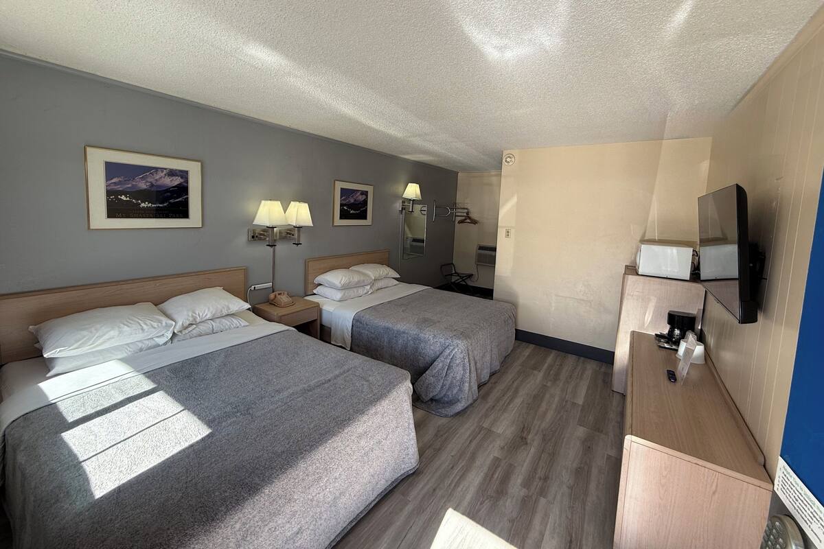 Quarto de hotel com duas camas, uma escrivaninha, televisão e espelho.