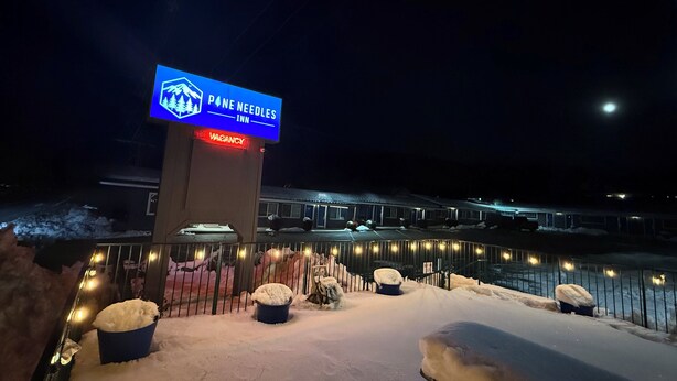 A snow-covered outdoor area with a sign for Pine Needles Inn, featuring a bench and a snow-covered planter. - Pine Needles Inn (Mount Shasta)