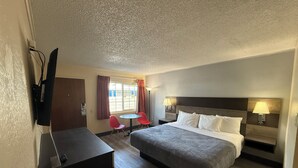 A hotel room with a bed, a desk, a chair, a TV, and a window with curtains. - Pine Needles Inn (Mount Shasta)