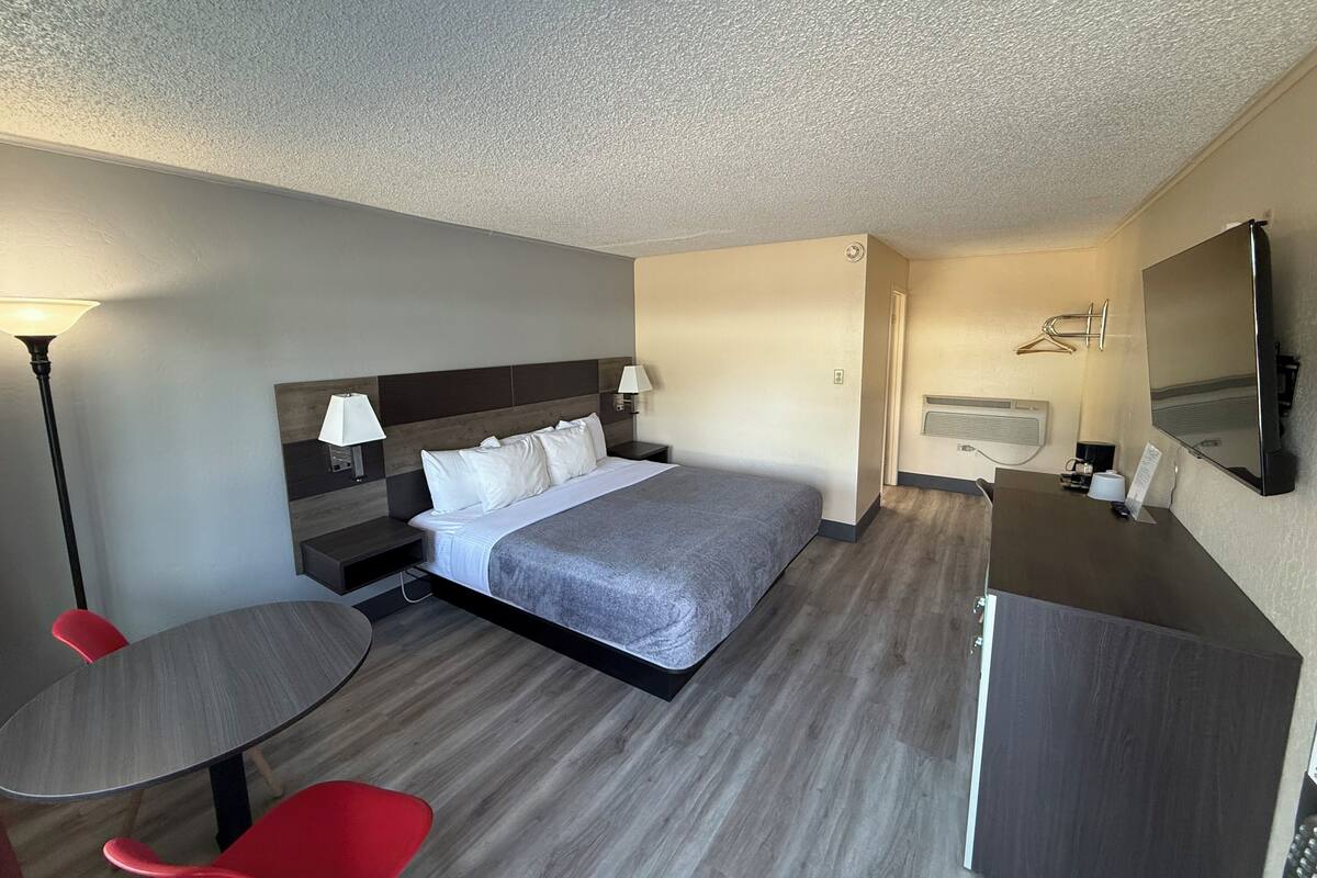 Quarto de hotel com cama, mesas de cabeceira, escrivaninha, cadeira, luminária, espelho e televisão de tela plana.