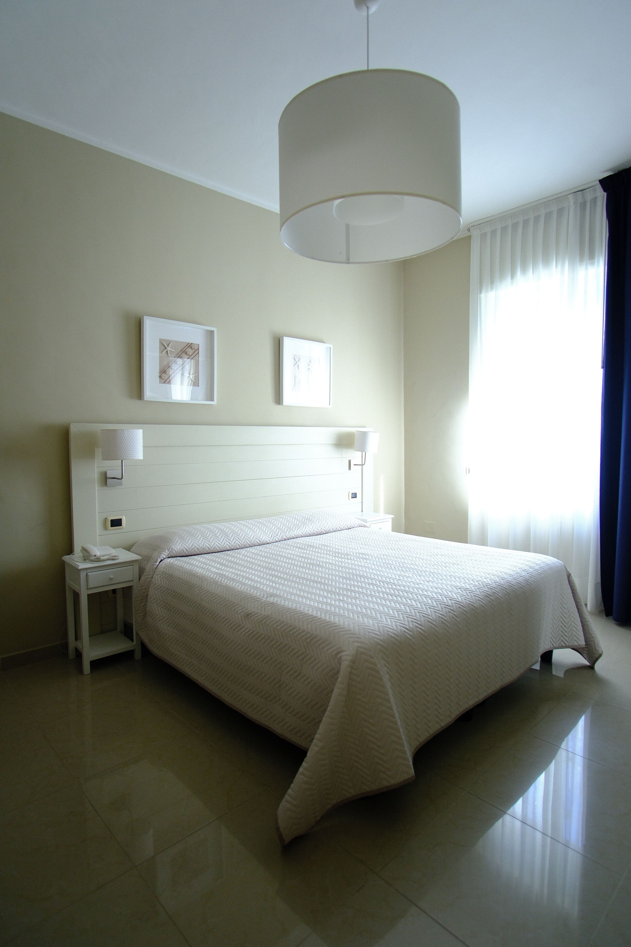 Un dormitorio ordenado con una cama grande, una mesita de noche con lámpara y dos cuadros en la pared.