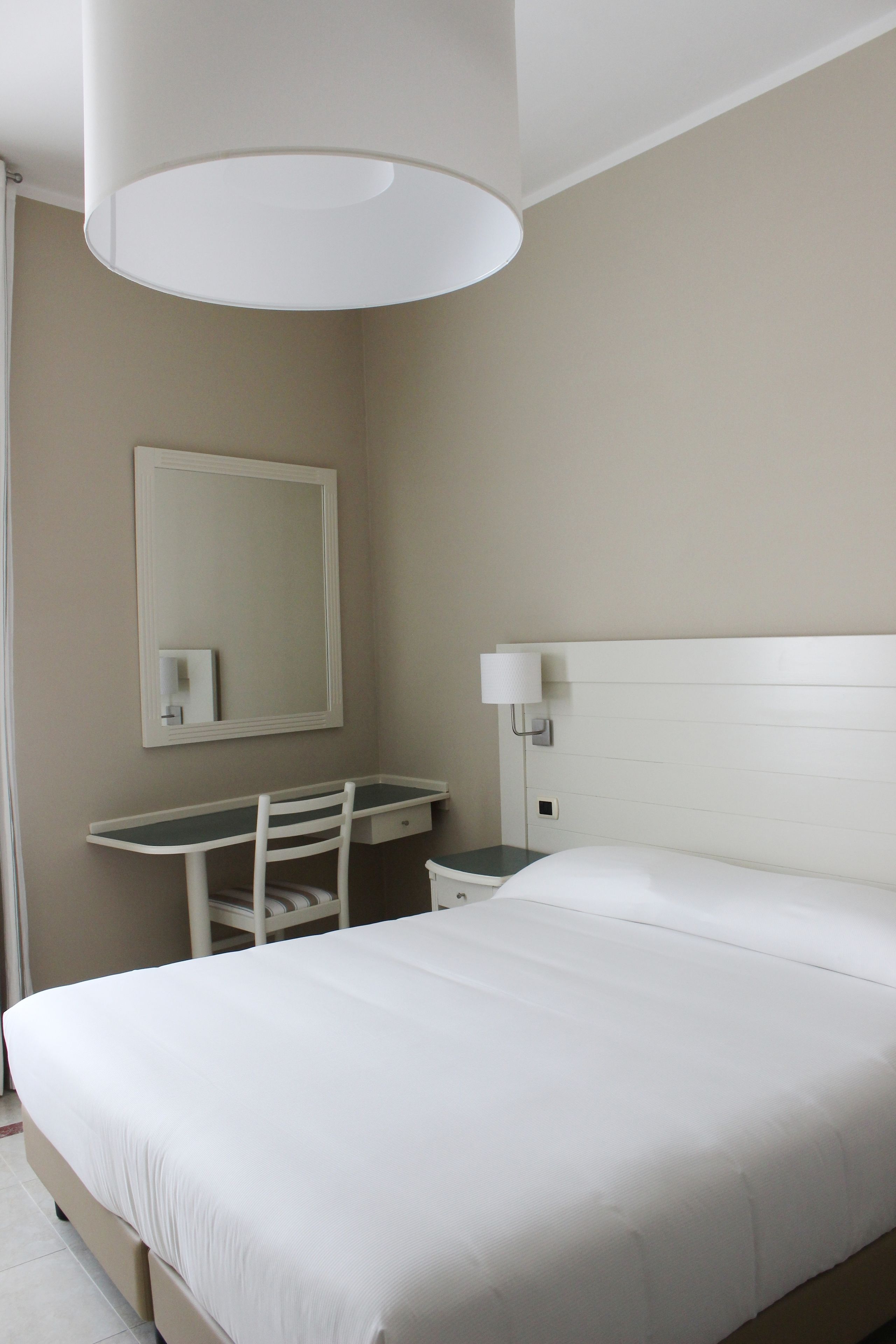 Une chambre d’hôtel avec un lit, un bureau, une chaise, un miroir et une lampe.