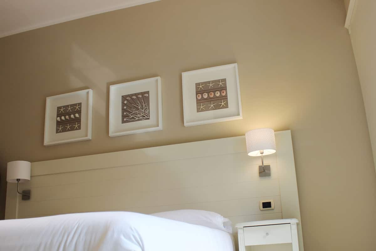 A hotel room with a bed, a nightstand, and three framed artworks on the wall.