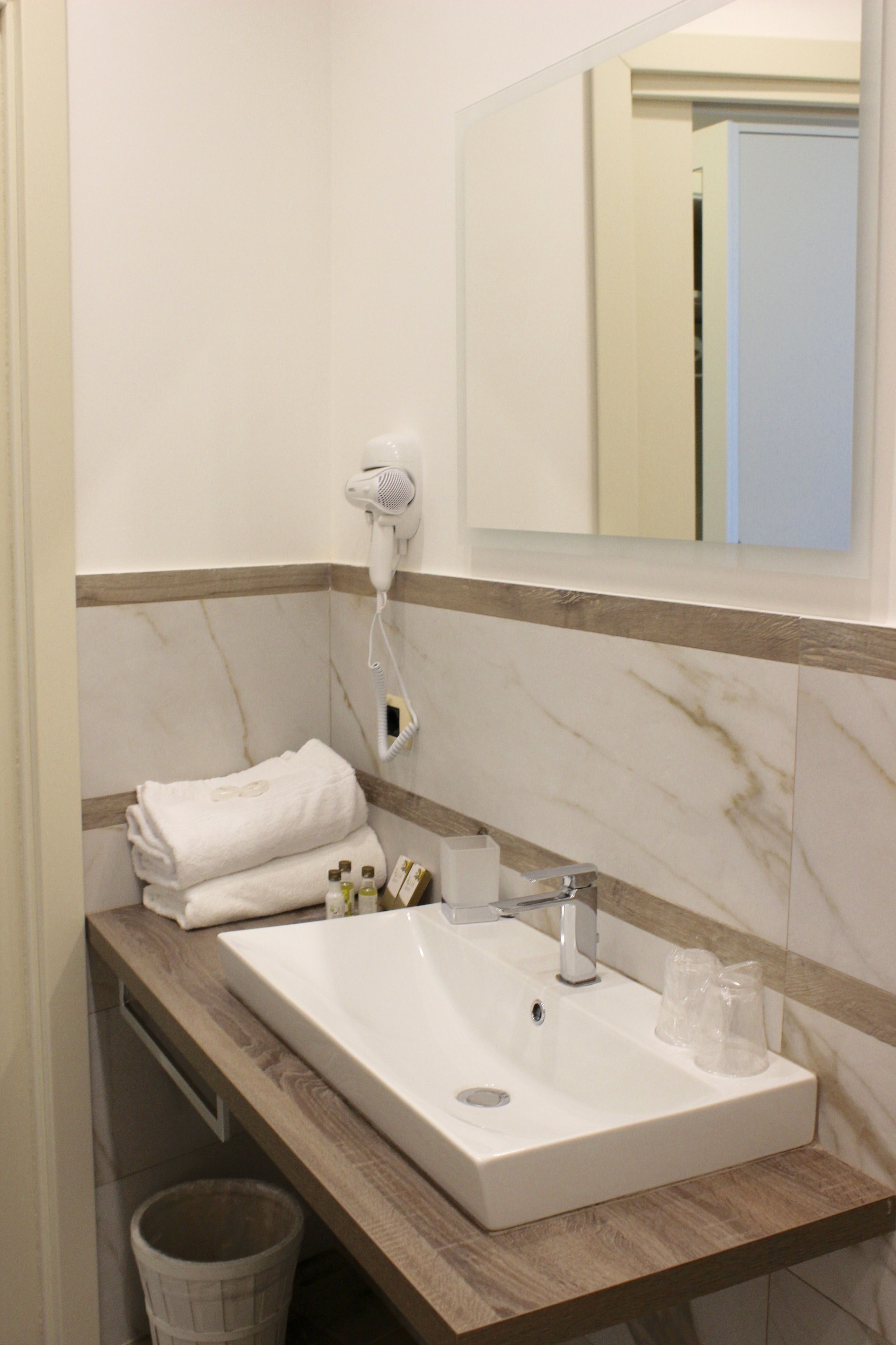 Un baño con pared de azulejos de mármol, encimera de madera, lavabo blanco, secador de pelo y espejo.