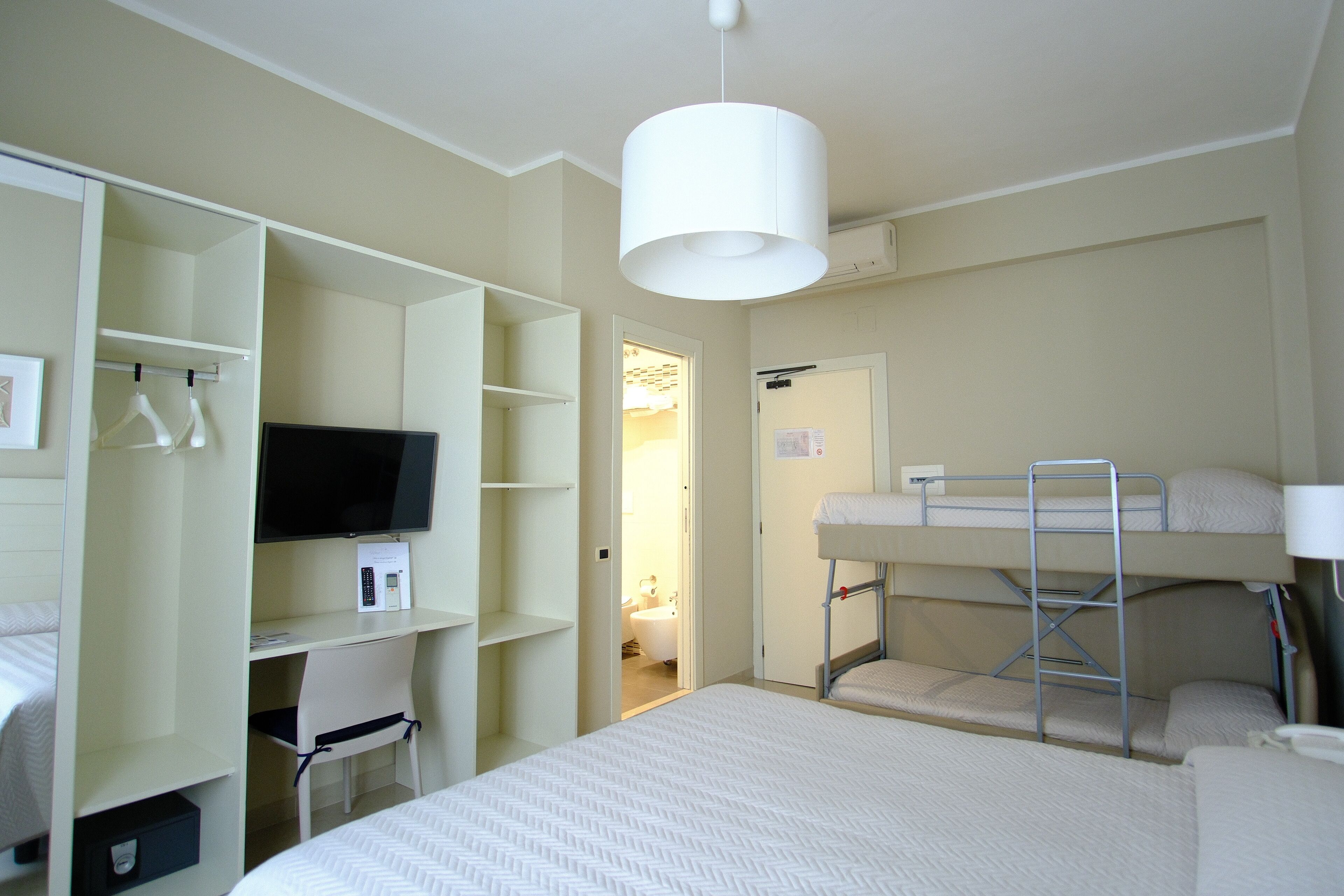 Une chambre d’hôtel compacte comprenant un lit superposé, un bureau avec une chaise, une télévision et une armoire.
