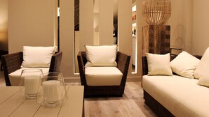 Una sala de estar moderna con muebles de mimbre, un sofá y un sillón con cojines. Hay una mesa de vidrio con dos candelabros de cristal.